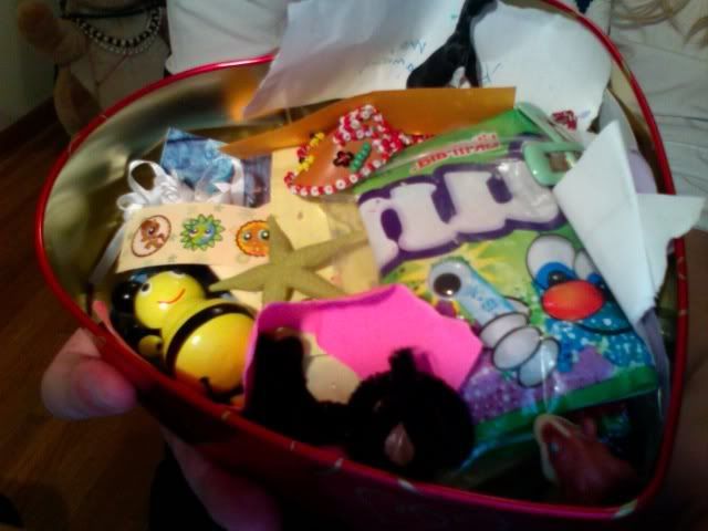 The same red box from the other picture, opened to reveal the contents. It contains several bits of paper, folded up letters, tiny toys, bits of candy and other odd things